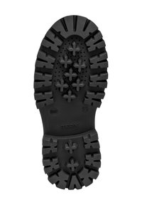 Suela de zapato de goma negra con un patrón de tracción robusto, acentos en forma de cruz y pequeñas perforaciones para transpirabilidad. Logo de la marca presente.