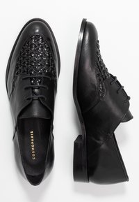 Chaussures en cuir noir à lacets avec un motif tissé sur le bout et un petit talon. Texture lisse et design minimaliste. Marque dorée à l'intérieur.