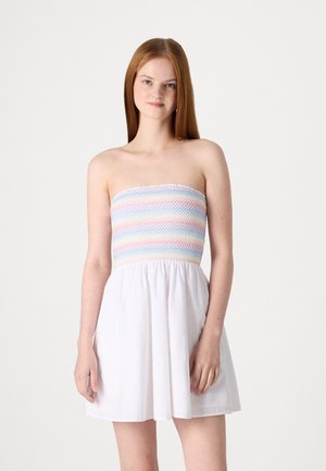 Robe sans bretelles avec un corsage smocké coloré à rayures horizontales et une jupe blanche évasée. Tissu doux avec une légère texture.