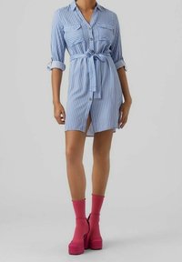 Různobarevné modro-bílé pruhované šaty s límečkem, s knoflíkovým zapínáním vpředu, dvěma náprsními kapsami, v pase uvázané, doplněné o jasně růžové platformové boty.