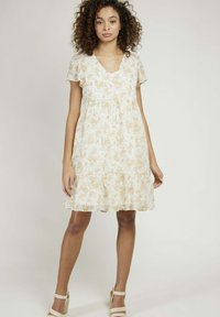 Robe à motif floral en crème clair avec des accents jaunes, décolleté en V, manches courtes et ourlet à volants, fabriquée en tissu léger et fluide.