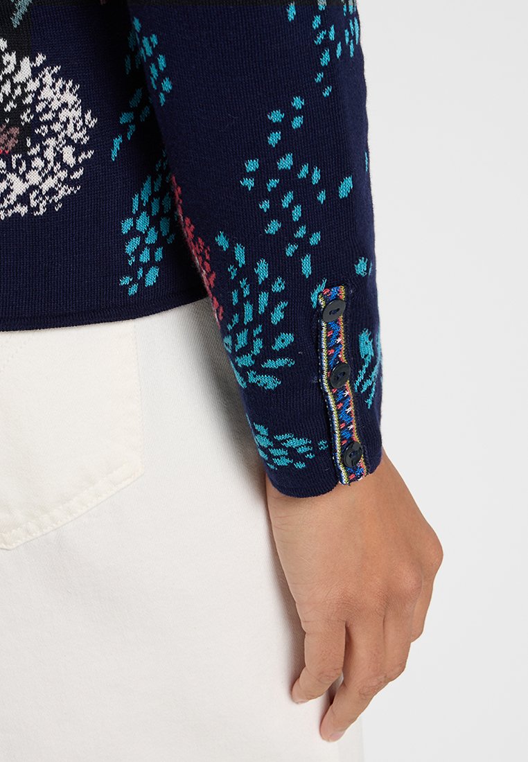 Maglione blu scuro con motivo floreale in turchese e rosa. Il polsino presenta bottoni decorativi e bordi multicolori. Il tessuto sembra essere lavorato a maglia.