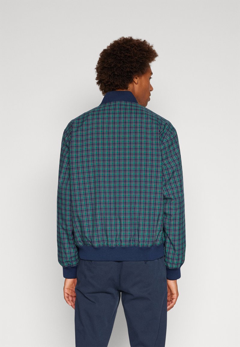 Veste bombardier à carreaux en bleu, vert et violet avec des poignets et une taille côtelés. Tissu léger avec une coupe décontractée.