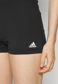 Şorturi atletice negre, realizate dintr-un material elastic, cu un logo Adidas alb pe partea stângă jos și cusături plate.
