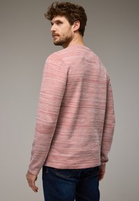 Chemise à manches longues avec un motif en rose et blanc chiné, dotée d'un col rond et d'une texture subtile ; associée à un jean bleu foncé.