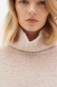 Maglione in morbido cachemire rosa chiaro, con colletto alto e piegato e superficie testurizzata. Primo piano del dettaglio del tessuto, che mette in evidenza l'aspetto morbido e soffice.