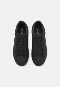 Baskets noires en matériau synthétique lisse, avec une pointe arrondie, un design à lacets et un détail de logo sur la semelle intérieure.