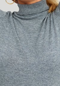 Helles graues Rollkragenpullover mit gerippter Textur, tailliertem Design und gerafften Details an den Schultern für zusätzliche Dimension.
