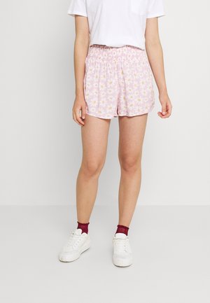 Lyserøde shorts med blomstermønster af tusindfryd, elastisk talje og afslappet pasform. Båret med en hvid T-shirt og sneakers.