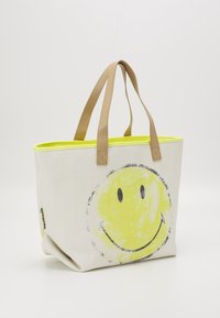 Sac fourre-tout en tissu blanc texturé avec un grand imprimé de smiley jaune, doté de poignées en cuir couleur tan et d'une doublure intérieure jaune néon.