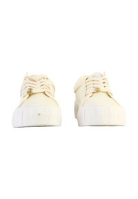White canvas sneakers with flat laces, round toe, and textured rubber soles. Features a minimalist design and a subtle brand logo on the side.
