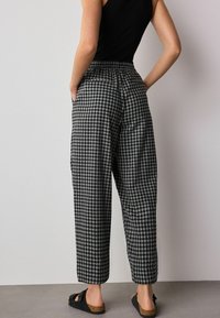 Black and white checkered high-waisted trousers with an elastic waistband, side pockets, and relaxed fit, paired with black sandals.