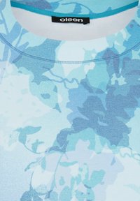 Helles blaues Oberteil mit floralem Muster in verschiedenen Blautönen. Rundhalsausschnitt mit kontrastierendem türkisfarbigen Saum. Strukturiertes Gewebe.