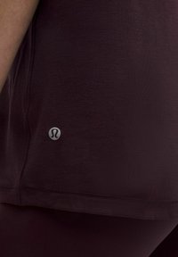 Burgundia spordipeadius, millel on sile tekstuur, lühike äär ja väike peegeldav logo vasakul küljel. Lähedalt vaade, näidates detaile.