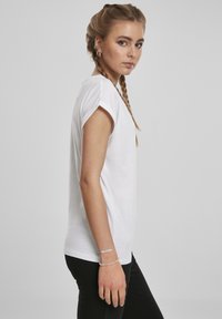 Valge lühikeste varrukatega t-särk, mille varrukate ääred on üles keritud ja millel on sile tekstuur. Kombineeritud mustade pükstega, mis esindavad lihtsat ja klassikalist disaini.