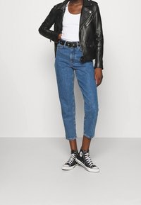 Chaqueta motera de cuero negro, camiseta sin mangas blanca, vaqueros azules de talle alto y zapatillas negras altas con cordones blancos. Estilo casual de ropa urbana.