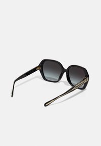 Ochelari de soare negri cu lentile hexagonale, nuanță gradient, ramă lucioasă și accente aurii pe brațe. Prezintă un design deosebit.
