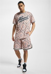 T-skjorte med korte ermer i rosa mønster og shorts, med svart logo, samt hvite og svarte striper, kombinert med høyhælte svarte sneakers.
