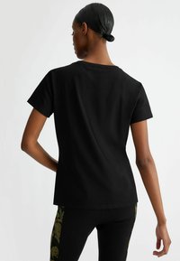 T-shirt nera a maniche corte realizzata in cotone morbido. Presenta un classico collo a giro e una vestibilità comoda, con un design posteriore semplice.