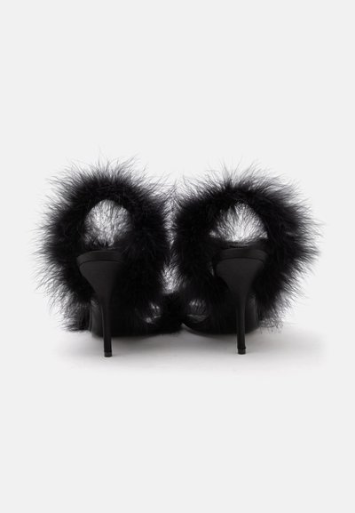 Paire de sandales noires à talons hauts avec une garniture de plumes duveteuses autour de la bride de cheville, vues de dos sur un fond blanc uni.