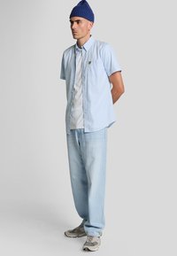 Camicia a maniche corte a quadri blu chiaro, t-shirt bianca sotto, jeans blu scoloriti, sneaker grigie e nere, berretto blu.
