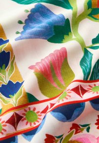 White fabric with colorful floral patterns in blue, pink, green, and red, featuring large flowers and decorative border designs.