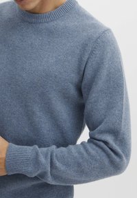 Blå strikkegenser med rund hals, ribbestrikkede mansjetter og hem, laget av myk ull, med en jevn tekstur og minimal detaljering.
