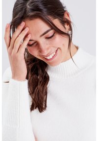 Pull en maille blanche douce avec un col à côtes haut et des manches ajustées. Le tissu semble chaud et confortable avec une texture lisse.