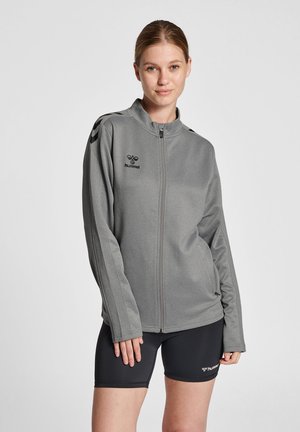Grå zip-jakke lavet af blødt stof, med høj krave, lange ærmer og sorte accentstriber på skuldrene. Hummel-logoet er vist.