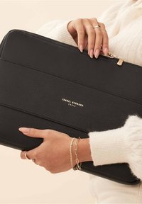 Sleeve per laptop in pelle nera con superficie texturizzata, hardware della cerniera dorato e logo impresso. Forma rettangolare con design minimalista.