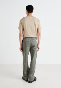 T-shirt en coton beige associé à un pantalon large olive. Le pantalon dispose de poches arrière et d'une petite étiquette logo près de la taille.