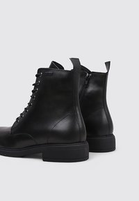 Bottines en cuir noir avec une finition lisse, à lacets à l'avant et fermeture éclair sur le côté ; conçues avec un bout rond et un petit talon.