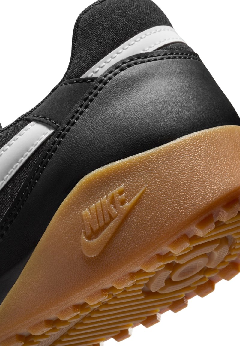 Sneaker nera con parte superiore in pelle e tessuto, dettagli bianchi e suola in gomma testurizzata. Presenta il logo Nike sulla suola.