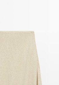 Primo piano di un tessuto in maglia beige con un delicato motivo a zigzag e cuciture ordinate lungo il bordo superiore.