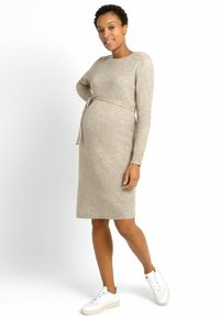 Abito premaman beige con maniche lunghe, una cintura in vita e un design lungo fino al ginocchio. Indossato con sneakers bianche, caratterizzato da una texture liscia.