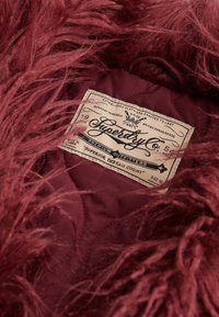 Bordeaux nepbont gevoerd jack met een gewatteerde satijnen voering. Beschikt over een geweven label met de merknaam "Superdry" en maat 10.