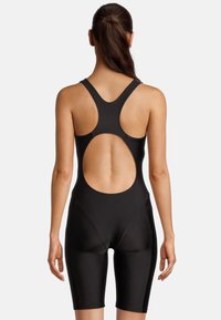 Maillot de bain noir avec un design à dos nageur et un dos circulaire ouvert. Présente une coupe ajustée et des jambes jusqu'aux genoux. Texture lisse.