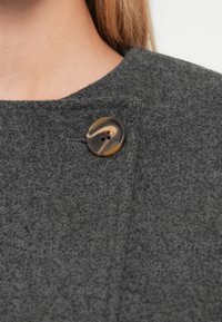 Γκρι υφασμάτινη υφή με στρογγυλό, μαρμάρινο κουμπί με δύο τρύπες, τοποθετημένο στον γιακά ενός ρούχου. Απλός και λειτουργικός σχεδιασμός.