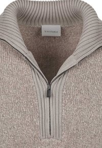 Light brown knitted sweater with half zipper and ribbed high collar, showing brand label inside collar.