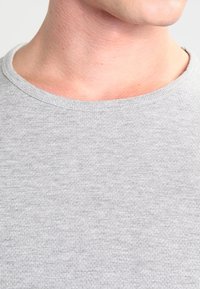 T-shirt grigio a collo tondo in un tessuto morbido e testurizzato. La vista ravvicinata mette in evidenza il colletto liscio e il delicato motivo del materiale.