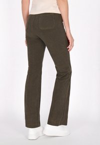 Corduroy broek in olijfgroen, met een flared ontwerp, een gestructureerd oppervlak en twee achterzakken, gecombineerd met witte sneakers.