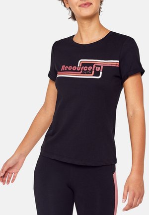 Femme portant un t-shirt noir à manches courtes avec le texte «Resourceful» et un motif rayé rose et blanc au niveau de la poitrine.