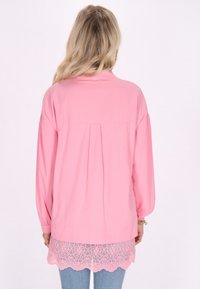 Top a maniche lunghe rosa realizzato in tessuto leggero. Presenta una schiena plissettata e un bordo in pizzo all'orlo, abbinato a jeans in denim blu.