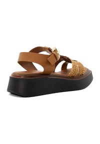 Sandal en cuir tan avec des accents tissés et une boucle, dotée d'une semelle épaisse en noir pour plus de hauteur et de stabilité.