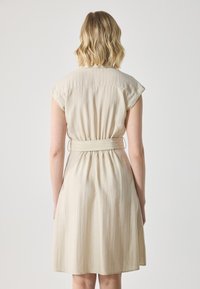 Beige, kortermet kjole med belte i midjen og subtile vertikale striper. Lett materiale med avslappet passform og utvidet skjørt.
