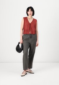 Top de punto corto color óxido con escote en V y lazo en la parte delantera, combinado con pantalones holgados de color gris oscuro y zapatos rosa suave. Incluye un bolso negro.