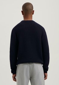 Marineblauwe geribde trui met lange mouwen, ronde halslijn en een ontspannen pasvorm, gecombineerd met lichtgrijze joggingsbroek. Geen zichtbare logo's of patronen.