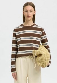 Camicia a maniche lunghe a righe nei colori marrone, crema e blu, abbinata a pantaloni beige con coulisse e una borsa intrecciata beige. Materiale in cotone morbido.