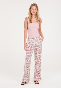 Lichtroze ribbel tanktop, gecombineerd met luchtige, gemusterde wijde broek met abstracte ontwerpen in roze, blauw en grijs. Flip-flops.