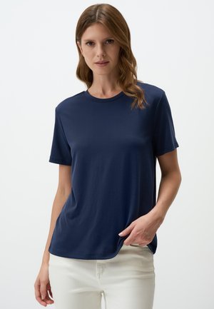 T-shirt blu navy a maniche corte realizzato in tessuto morbido, con scollatura a girocollo e vestibilità comoda, abbinato a pantaloni di colore chiaro.